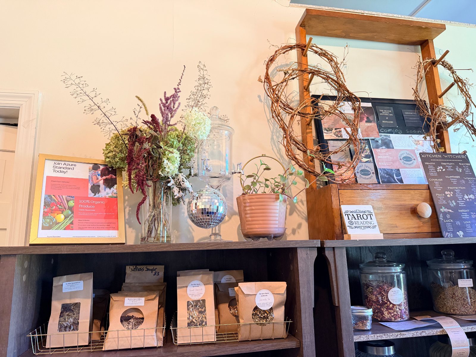 The tea shelf: dried flowers and a grapevine wreath above, bags of loose tea and jars of bulk herbs on the shelf below